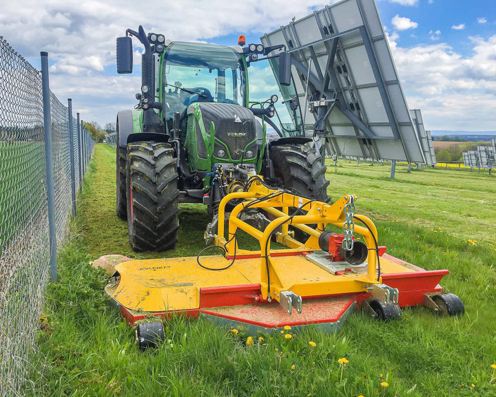 Fendt-tractor met Ilmer EMG strokenmaaier maait het gras tussen de zonnepanelen op een zonnepark