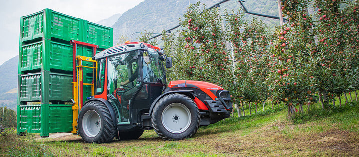 Smalspoortractor met Ilmer K2-D hefmast vervoert gestapelde fruitkisten in de appelboomgaard