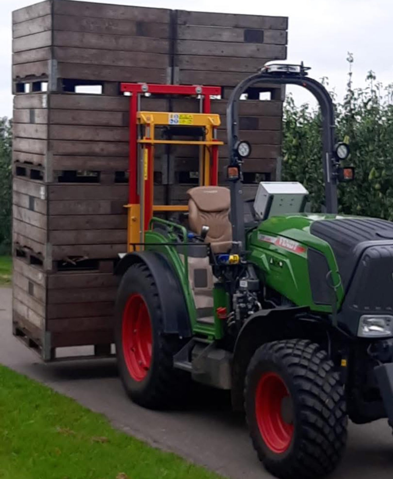 Fendt smalspoortractor met Ilmer hefmast en fruitkisten op het erf